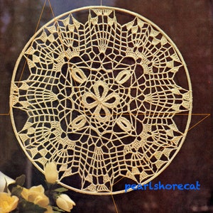May include: A beige crocheted doily with a circular design. The doily has a delicate, intricate pattern with a floral motif in the center.