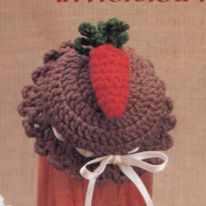 May include: A brown crocheted jar lid with a crocheted carrot and green leaves on top. The lid is tied with a white ribbon.