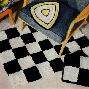 May include: A black and white checkered rug and matching pillow set. A triangular pillow with yellow, white, and black accents sits on a gray chair. The rug and pillow have a textured, shaggy appearance.