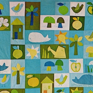 May include: A patchwork quilt featuring a repeating pattern of whimsical illustrations. The design includes houses, birds, apples, mushrooms, whales, suns, and watering cans in shades of green, yellow, blue, and white. The quilt is made of squares.