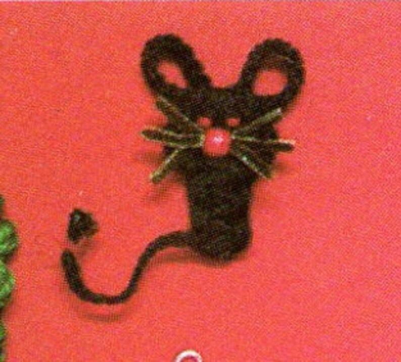 May include: A black crocheted mouse with a red button nose and green yarn whiskers. The mouse has a long, curled tail.