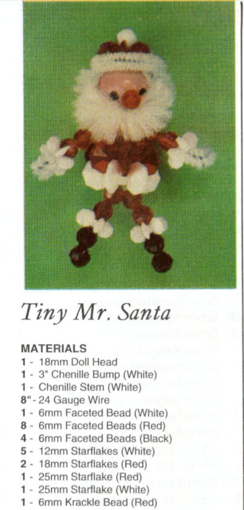 Op de afbeelding: Een handgemaakte Tiny Mr. Santa figuur, gemaakt van een poppenhoofd, chenille, draad, kralen en sterren. De figuur heeft een witte baard en hoed, een rode jas en zwarte en witte accenten. De tekst "Tiny Mr. Santa" is zichtbaar.