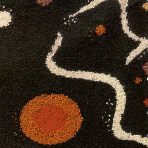 May include: A close-up of a black, textured rug with white, orange, and red circular shapes. The rug has a unique, abstract design.