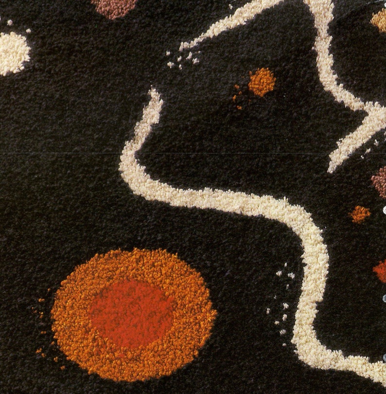 May include: A close-up of a black, textured rug with white, orange, and red circular shapes. The rug has a unique, abstract design.