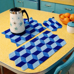 Peut inclure: Une cafetière blanche et argentée avec une poignée noire est posée sur un chemin de table à motifs géométriques bleus et bleu clair. Des dessous de plat assortis et un bol d'oranges sont également sur la table jaune.