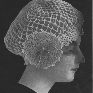 Puede incluir: Un sombrero blanco de ganchillo con un delicado diseño de encaje y borlas. El sombrero se lleva en la cabeza de un maniquí.