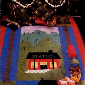 May include: A colorful Christmas tree skirt featuring a train station design. The skirt has a red border, blue and green panels, and a central image of a red station with the word "STATION". Decorative toy train cars and animals are also present.