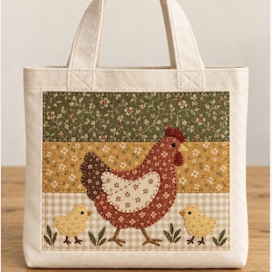 Puede incluir: Un bolso de tela color crema con una aplicación rectangular en la parte frontal. La aplicación muestra una gallina marrón con un ala de flores blancas y dos pollitos amarillos, sobre franjas horizontales de tela verde, amarilla y de cuadros vichy beige.