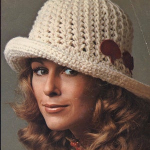 Pu&ograve; includere: Cappello all'uncinetto color crema con corona arrotondata e piccola tesa. Il cappello presenta due accenti color amaranto. Il cappello &egrave; in stile vintage.