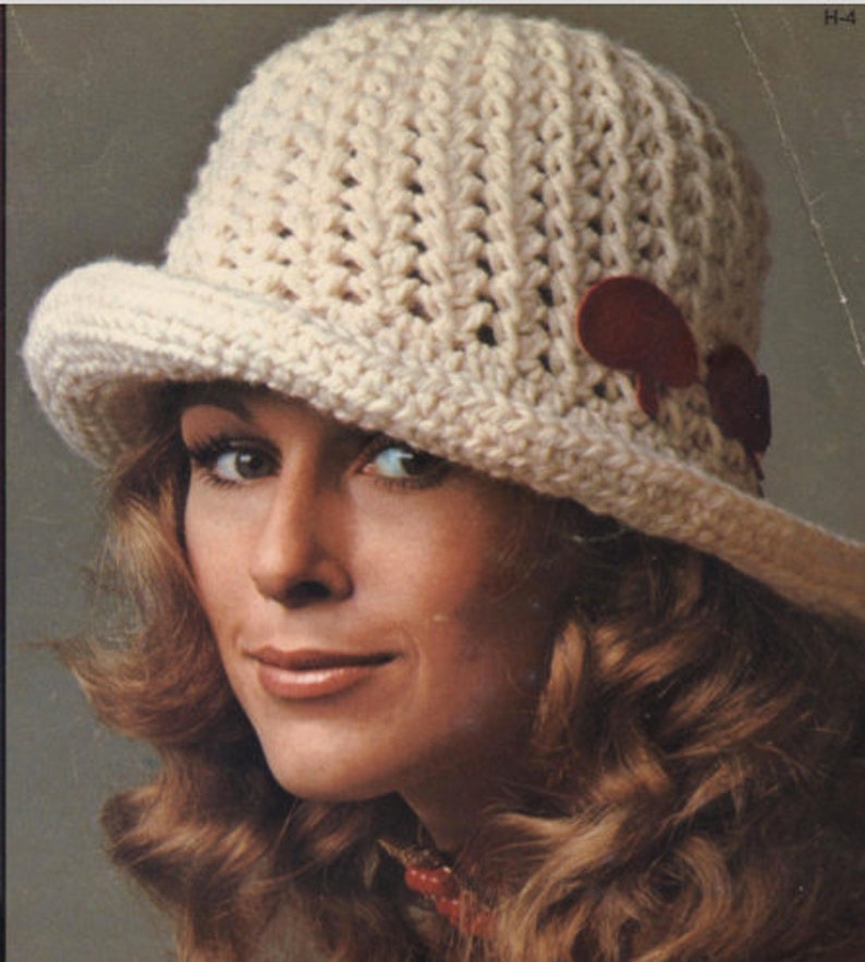 Pu&ograve; includere: Cappello all'uncinetto color crema con corona arrotondata e piccola tesa. Il cappello presenta due accenti color amaranto. Il cappello &egrave; in stile vintage.