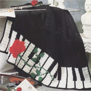 May include: Black crochet blanket with a white and black piano key border and a red rose with green leaves.