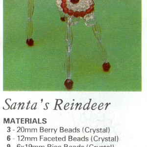 Op de afbeelding: Een handgemaakt rendierornament gemaakt van heldere kristallen kralen, rode kralen en goudkleurige kralen. Het rendier heeft een rode kraag en een gouden kralen geweidesign. De tekst "Santa's Reindeer" is zichtbaar.
