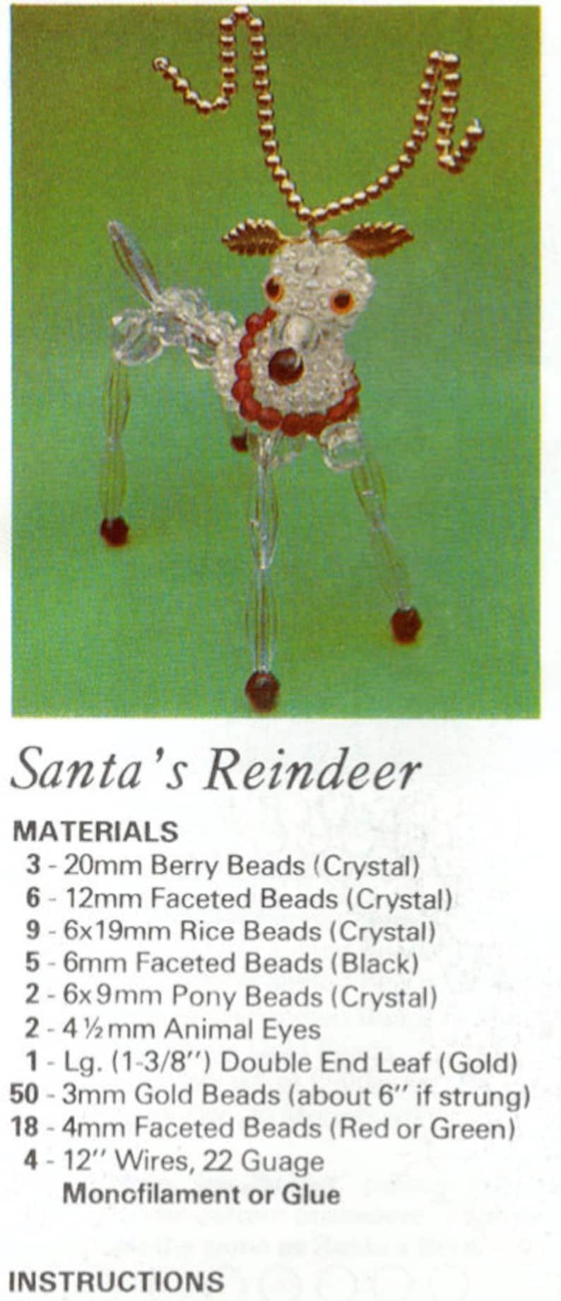 Op de afbeelding: Een handgemaakt rendierornament gemaakt van heldere kristallen kralen, rode kralen en goudkleurige kralen. Het rendier heeft een rode kraag en een gouden kralen geweidesign. De tekst "Santa's Reindeer" is zichtbaar.