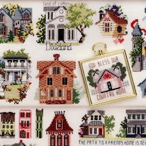 May include: A cross-stitch sampler featuring various house designs, including a framed piece with the text "GOD BLESS OUR COUNTRY HOME." Other houses are labeled "Dixieland" and "land of cotton." The phrase "THE PATH TO A FRIEND'S HOME IS NEVER LONG" is also present.