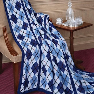 Puede incluir: Una manta tejida con un patrón de rombos en azul, azul claro y blanco, con finas líneas negras y rojo oscuro entrecruzadas. La manta está colocada sobre una silla, mostrando un diseño de diamantes repetido con un borde azul oscuro sólido.