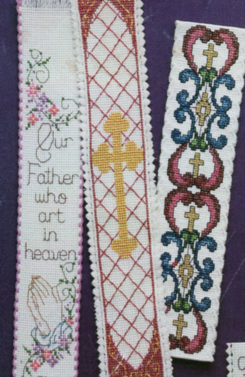 Peut inclure: Trois marque-pages en tissu blanc avec broderie au point de croix. Le premier marque-page porte le texte "Notre P&egrave;re qui es aux cieux" et une paire de mains en pri&egrave;re. Le deuxi&egrave;me marque-page a une croix jaune sur un motif de grille rouge et blanche. Le troisi&egrave;me marque-page a un motif floral bleu et vert avec un c&oelig;ur rouge et une croix.