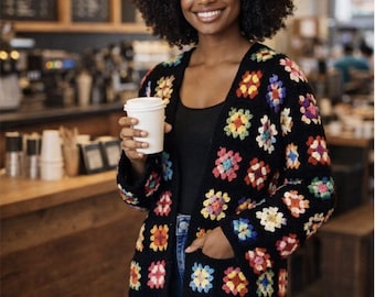 May include: A black open-front cardigan featuring a repeating pattern of multi-colored crochet granny squares in shades of red, yellow, blue, pink, and white, with long sleeves and two front pockets, worn over a black top and blue jeans.