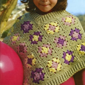 Pode incluir: Uma menina pequena usando um poncho de crochê verde com um padrão quadrado de flores amarelas, rosa e roxas. O poncho é usado sobre uma camisa vermelha. A menina está segurando uma bola rosa grande.