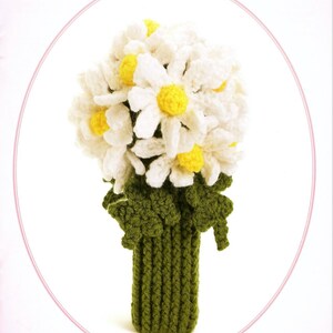 May include: A crocheted bouquet of white daisies with yellow centers, arranged in a green crocheted vase.