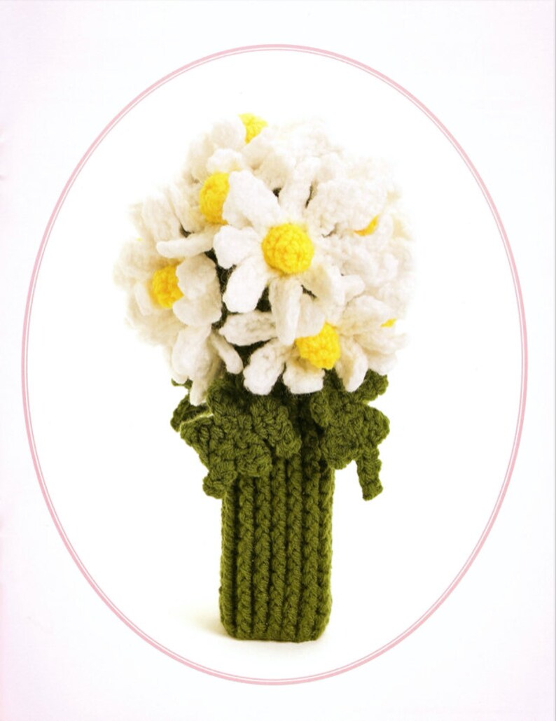 May include: A crocheted bouquet of white daisies with yellow centers, arranged in a green crocheted vase.