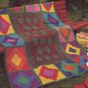May include: A colorful crocheted blanket with a geometric pattern. The blanket is made up of squares with different colors and designs. The blanket is lying on a wooden bench with green grass in the background.