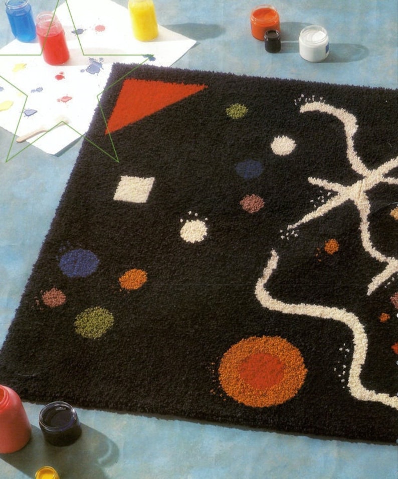 May include: A black rug with a white abstract design and colorful dots. The rug is surrounded by paint pots and a white sheet of paper with paint splatters.