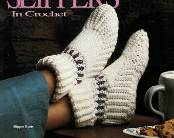 May include: A pair of white crochet slipper boots featuring a ribbed texture and a decorative band with small red and green accents. The text SLIPPERS In Crochet and Slipper Boots is visible at the top and bottom of the image.