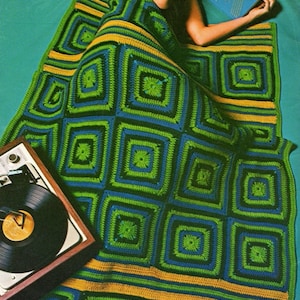 Puede incluir: Una manta de ganchillo de granny square en verde, azul y amarillo. La manta está doblada y drapeada sobre una persona que está tumbada sobre un fondo turquesa. Un tocadiscos está en primer plano.