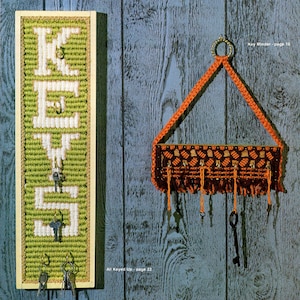 May include: A green and white yarn craft with the word "KEYS" spelled out. A brown and orange yarn key holder with a checkered pattern hangs on a blue wall. The text "Key Minder - page 16" is printed above the key holder. The text "All Keyed Up - page 22" is printed below the key holder.