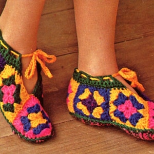 Può includere: Un paio di pantofole all'uncinetto colorate con un motivo a quadrati della nonna in tonalità di rosa, giallo, verde, blu e viola. Le pantofole hanno un laccio alla caviglia.