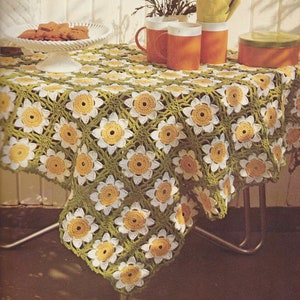 May include: A crocheted tablecloth with a green and white daisy pattern. The tablecloth is laid on a table with three orange mugs and a green container.