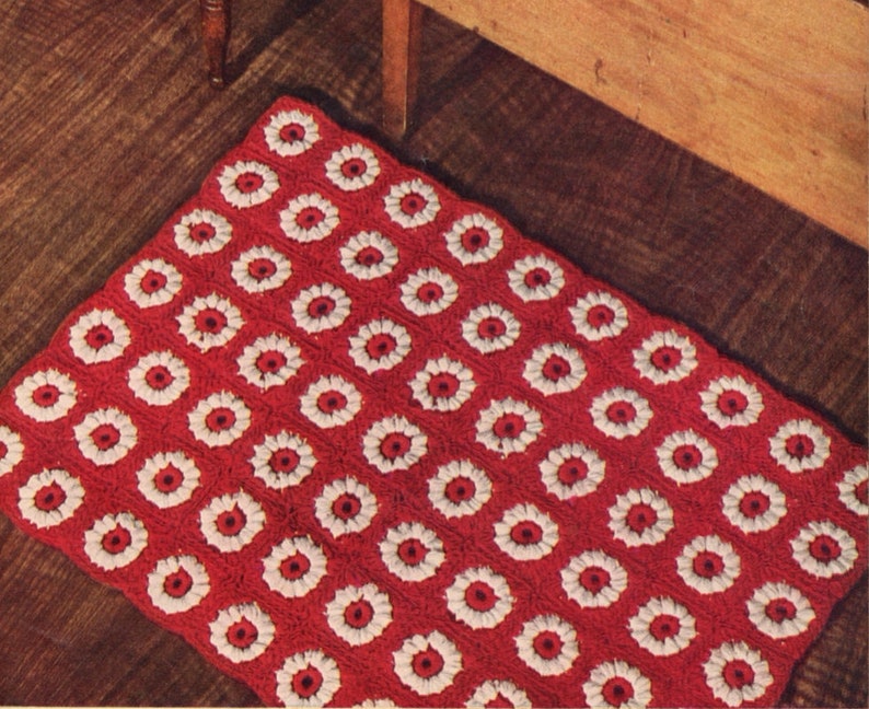 May include: A red and white crocheted rug with a floral pattern. The rug is made of yarn and has a square shape.