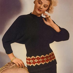 Op de afbeelding: Een zwarte gebreide top en rok set in vintage stijl. De top heeft een decoratief rood en goud geometrisch patroon in de taille. Het model draagt een gouden armband en ring. De achtergrond is een zachte, neutrale kleur.