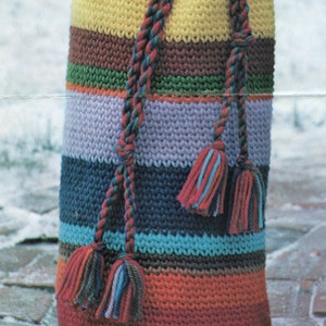 K&ouml;nnte beinhalten: Eine bunte geh&auml;kelte Tasche mit einem gestreiften Muster und langen Quasten. Die Tasche ist aus verschiedenen Blaut&ouml;nen, Gr&uuml;n-, Rot-, Orange-, Gelb- und Braunt&ouml;nen gefertigt.