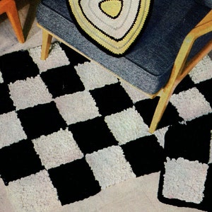 May include: A black and white checkerboard rug with a matching square accent rug. The rug is made of a textured material. A blue chair with a triangular, crocheted pillow is in the background.
