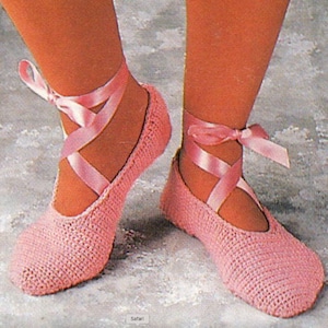 May include: Pink crocheted ballet slippers with satin ribbon ties. The slippers are worn on a pair of feet.
