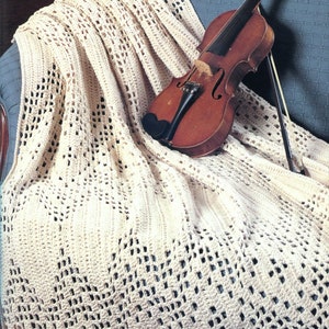 May include: A white crocheted throw blanket with a delicate openwork pattern, draped over a blue armchair with a violin resting on top.