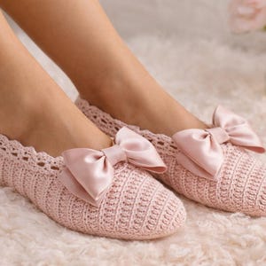 May include: A pair of light pink crocheted slippers with a scalloped edge and a large satin bow on each. The slippers are on a fluffy, light pink surface, suggesting comfort and relaxation. The overall theme is cozy and feminine.
