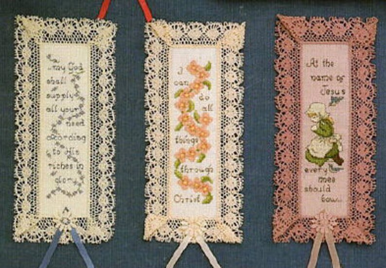 May include: Three handmade bookmarks with lace trim. The first bookmark is white with a floral design and the text "May God supply all your need according to His riches in glory". The second bookmark is white with a floral design and the text "I can do all things through Christ". The third bookmark is pink with a floral design and the text "At the name of Jesus every knee should bow".