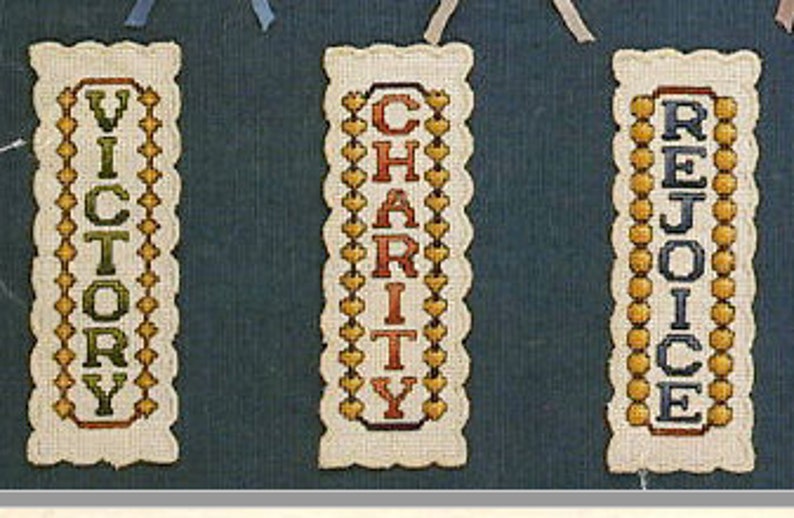 May include: Three embroidered bookmarks with scalloped edges. The bookmarks are white with yellow, green, and blue embroidery. The words "Victory", "Charity", and "Rejoice" are embroidered on the bookmarks.