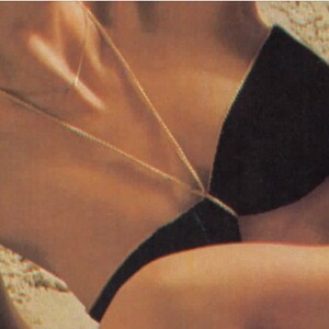 Puede incluir: Primer plano del pecho de una mujer que lleva un top de bikini negro con un collar de cadena dorada.
