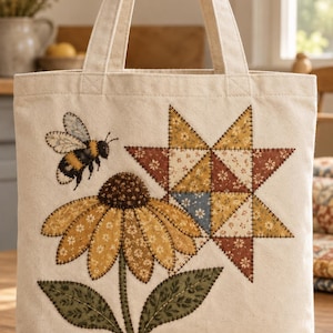 May include: A cream-colored canvas tote bag featuring an appliqued design of a yellow coneflower, a flying bumblebee, and a multi-colored patchwork star. The fabric elements are attached with visible dark brown decorative stitching.