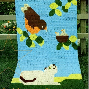Puede incluir: Una manta de ganchillo con fondo azul que presenta un petirrojo en una rama, un nido con dos pájaros y un gato blanco tumbado en la hierba. La manta está hecha con cuadrados de colores y tiene un estilo vintage.