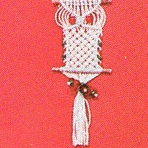 May include: White macrame owl wall hanging with a tassel. The owl has a diamond pattern on its body and a simple design for its eyes.