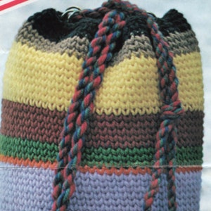 K&ouml;nnte beinhalten: Eine gestreifte geh&auml;kelte Kordeltasche mit einem geflochtenen Band. Die Tasche ist in verschiedenen Farben gefertigt, darunter Gelb, Braun, Gr&uuml;n, Orange und Lila.