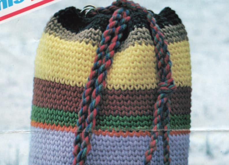 K&ouml;nnte beinhalten: Eine gestreifte geh&auml;kelte Kordeltasche mit einem geflochtenen Band. Die Tasche ist in verschiedenen Farben gefertigt, darunter Gelb, Braun, Gr&uuml;n, Orange und Lila.