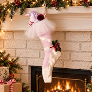 May include: A Christmas stocking shaped like a ballet pointe shoe in pale pink and cream satin. The top features a white tulle ruffle, a small unicorn figurine with a braided mane, a dark red pom-pom, and a candy cane. A holly sprig adorns the side.