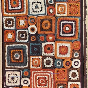 Op de afbeelding: Een gehaakt deken met een patchwork ontwerp met vierkanten en cirkels in tinten oranje, bruin, wit en blauw.