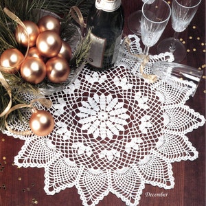 May include: White crocheted doily with a starburst design, surrounded by gold Christmas baubles, a bottle of champagne, and champagne glasses on a wooden table. The doily has the word "December" written on it.