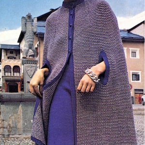 Puede incluir: Una capa de punto de color morado y blanco con cuello alto y cierre de botón. La capa tiene mangas largas con una abertura en el codo.